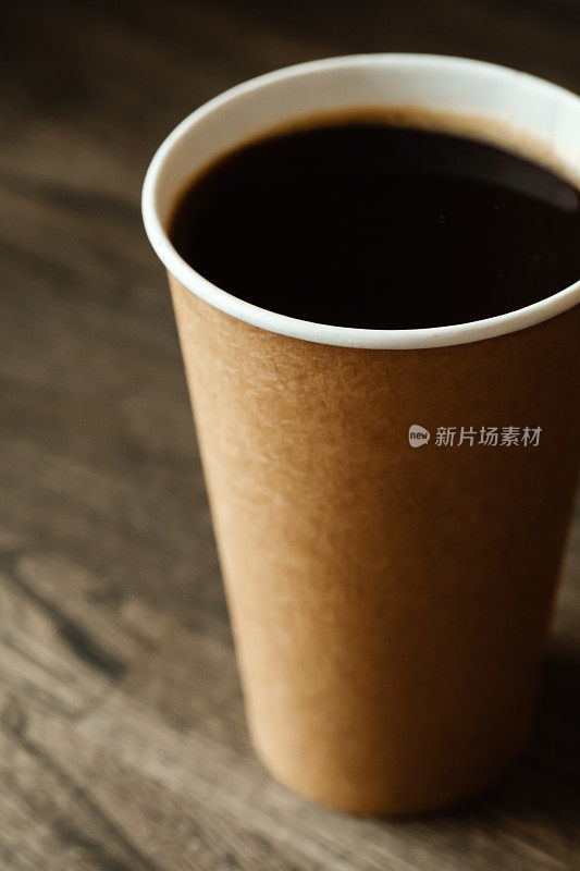 Paper cup with black freshly brewed coffee on a wooden table in a coffee shop. Ð¡up of hot coffee in confectionery shop or coffee in pub, bar, restaurant.